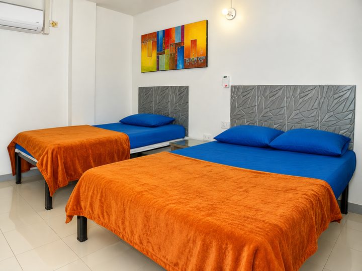 Habitación con una cama doble y una sencilla, sábanas azules y cobijas naranjas