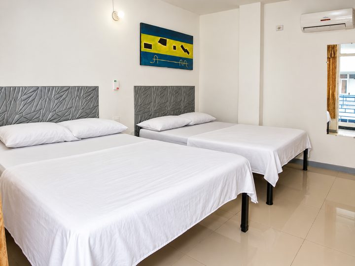 Habitación con dos camas dobles, cuadro azul y amarillo y aire acondicionado