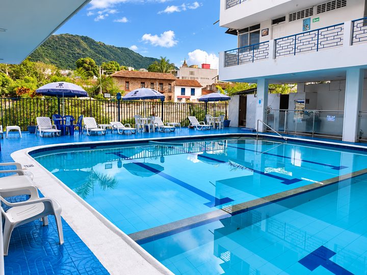 Piscina con sombrillas, asoleadoras y casas coloniales de Honda al fondo